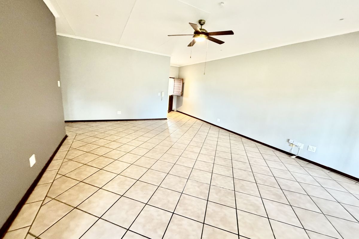 A spacious, empty living area featuring neutral walls, tiled flooring, and a ceiling fan, providing a versatile blank canvas for interior design.