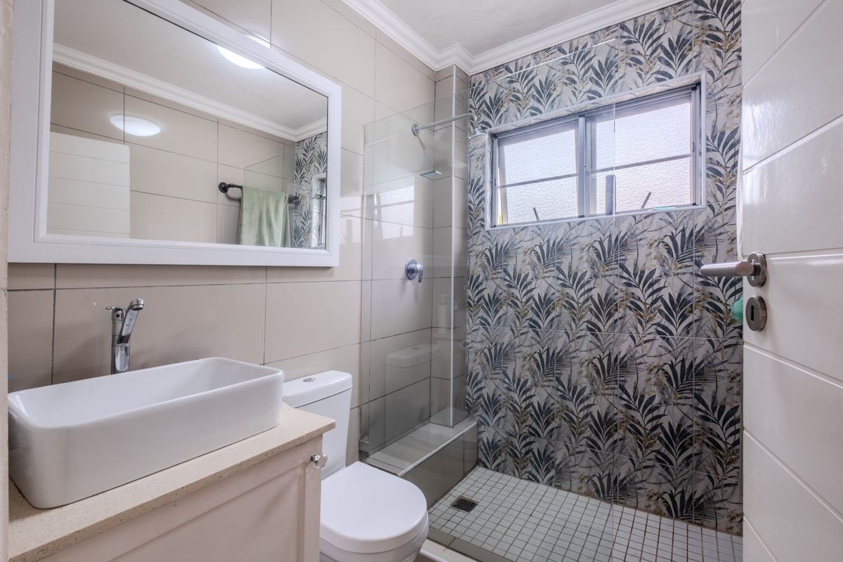 Modern bathroom featuring a vessel sink, vanity cabinet, toilet, and a glass-enclosed shower with decorative patterned wall tiles.
