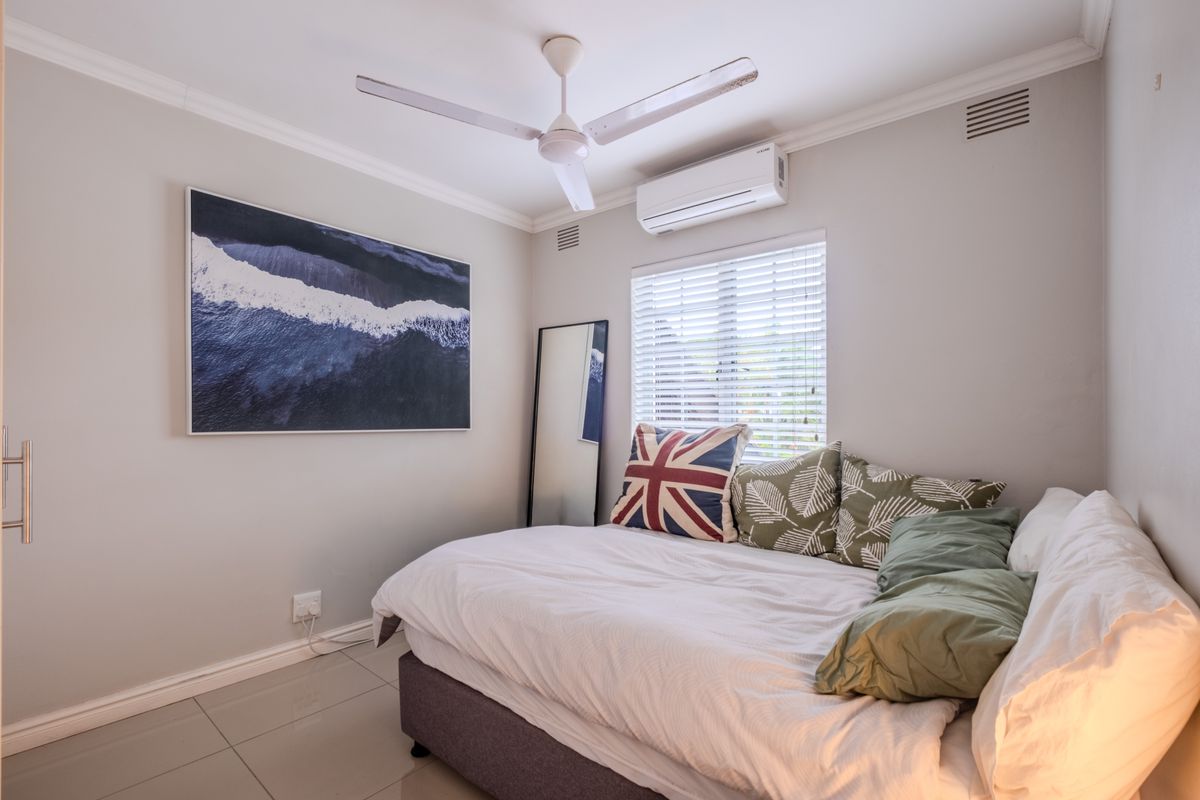A well-maintained bedroom featuring tiled flooring, a ceiling fan, and a split-system air conditioner for climate control.
