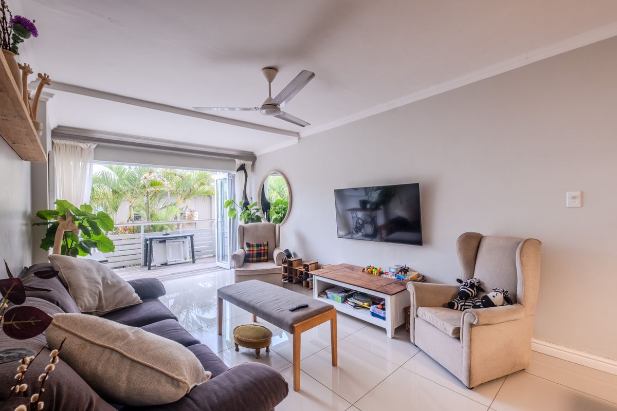 Bright living room featuring polished tile flooring, a ceiling fan, and large sliding glass doors providing seamless access to an outdoor balcony area.