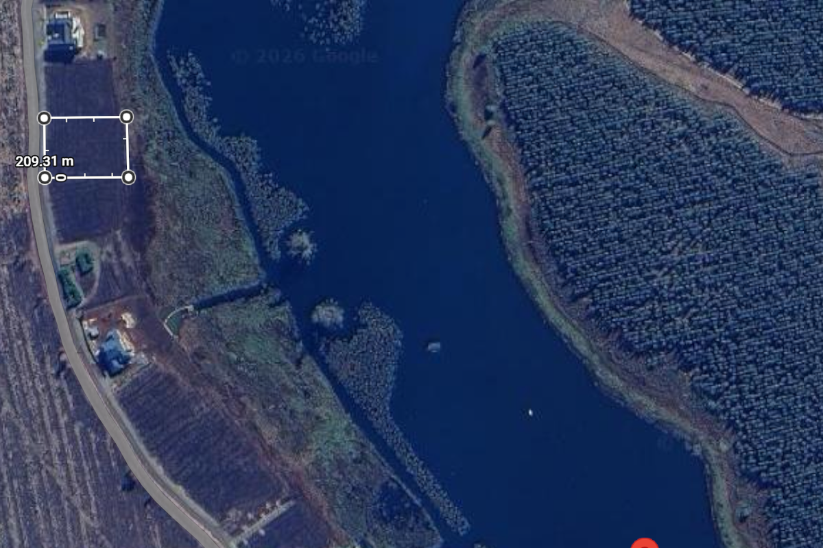 Aerial view of a vacant residential plot situated adjacent to a large dam and natural landscape.
