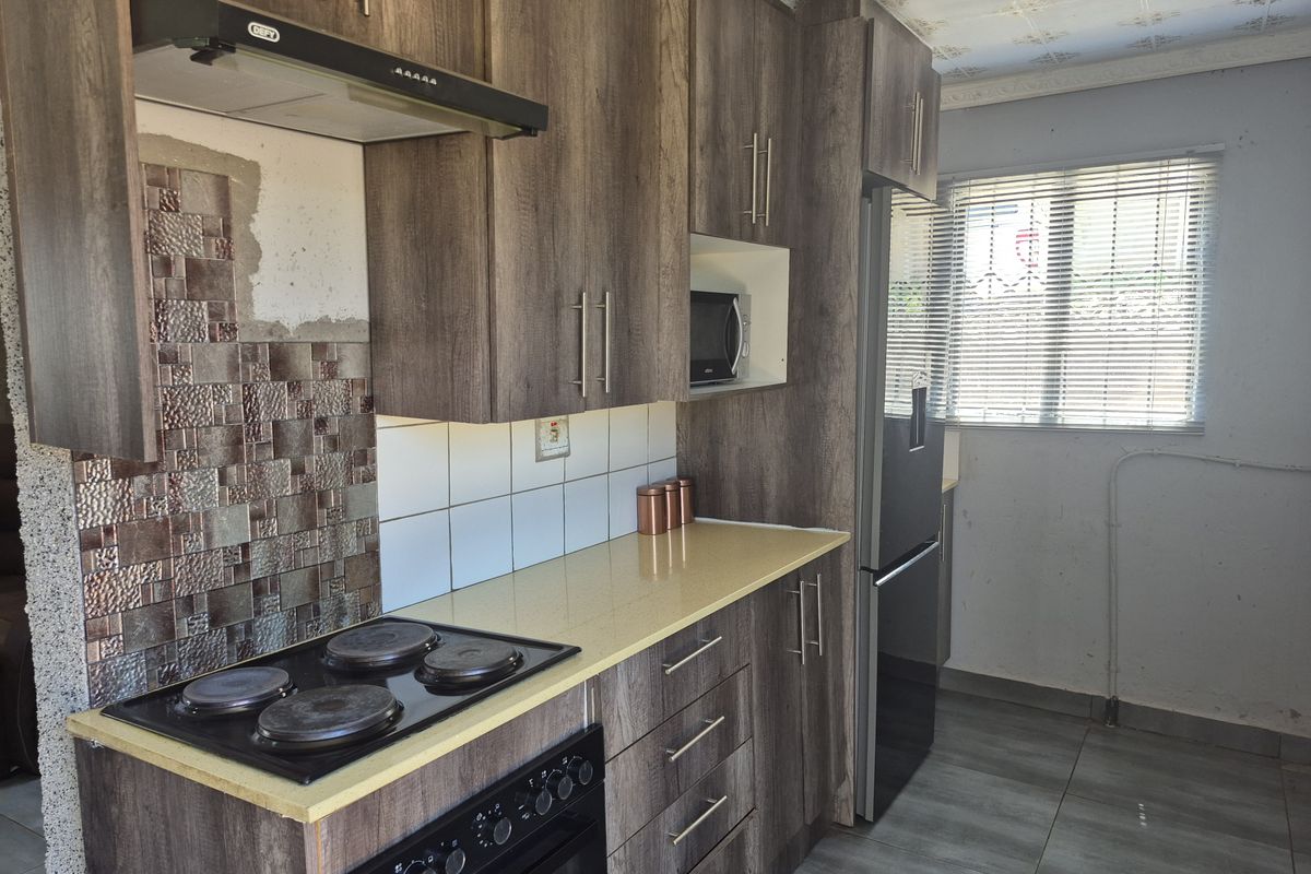 A functional kitchen featuring wood-look cabinetry, a built-in electric stove with extractor fan, tiled backsplash, and tiled flooring.