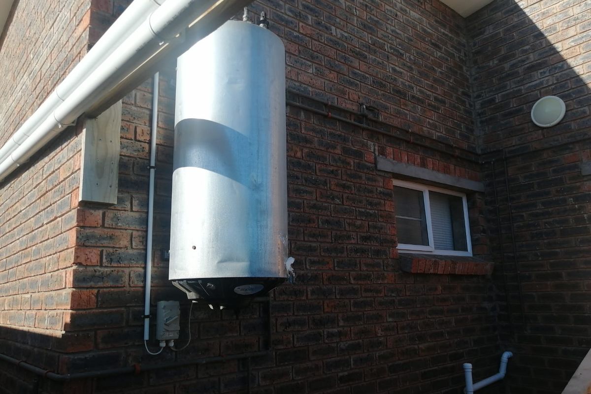 Exterior view of a brick apartment wall featuring an externally mounted geyser unit and drainage downpipe.