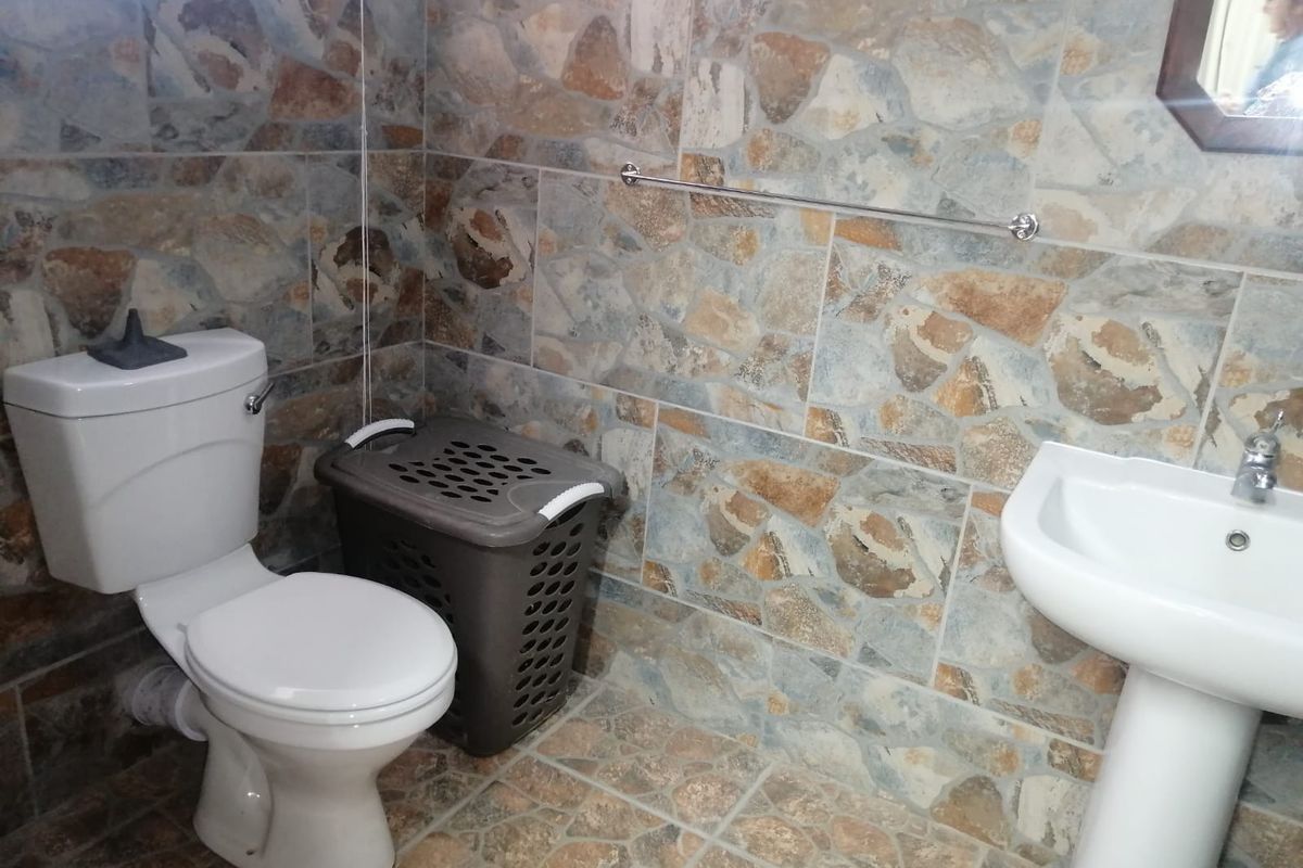 A functional bathroom featuring stone-look wall and floor tiling, a pedestal basin, and a standard toilet.