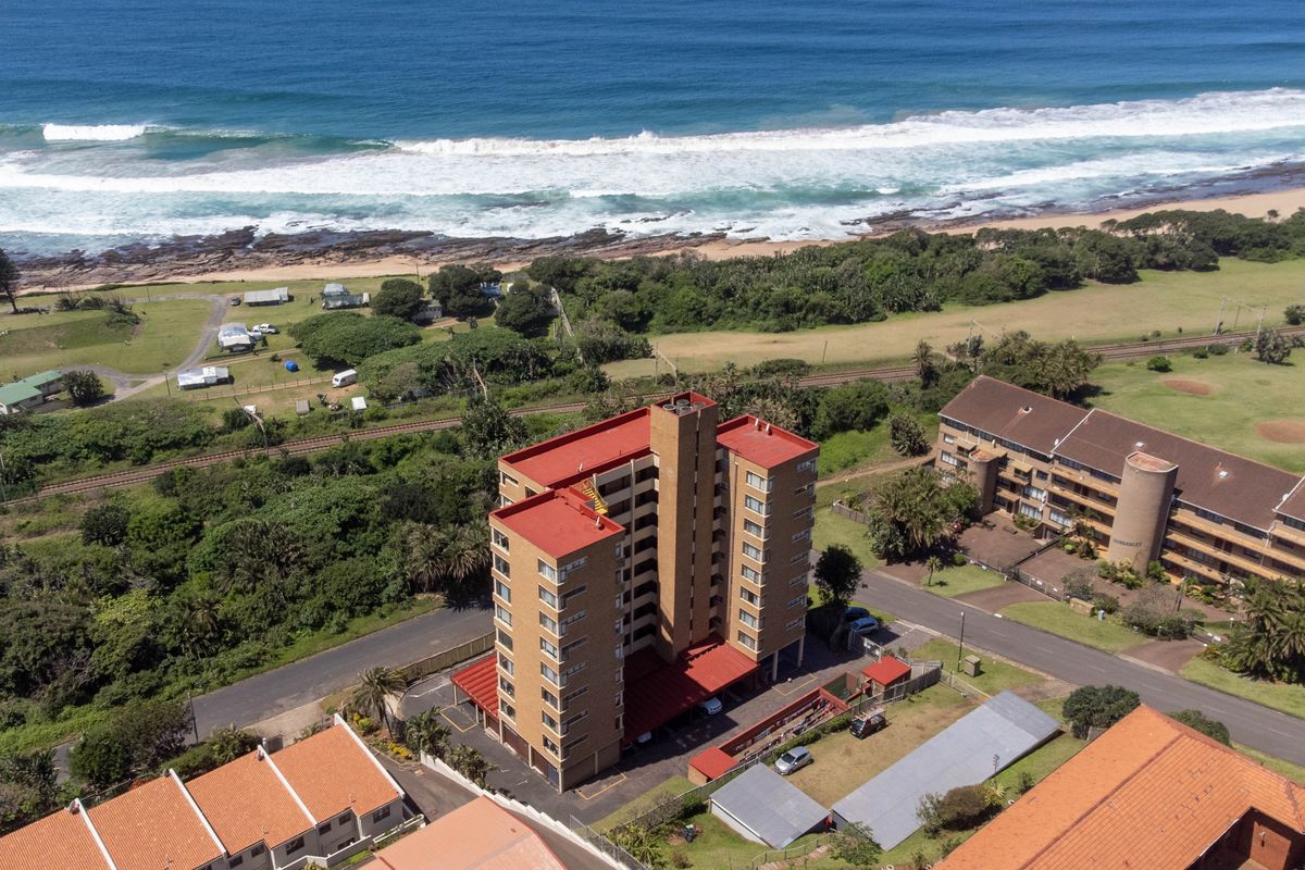 Aerial view of a multi-story brick apartment building situated in a coastal location with proximity to the beach and surrounding residential infrastructure.