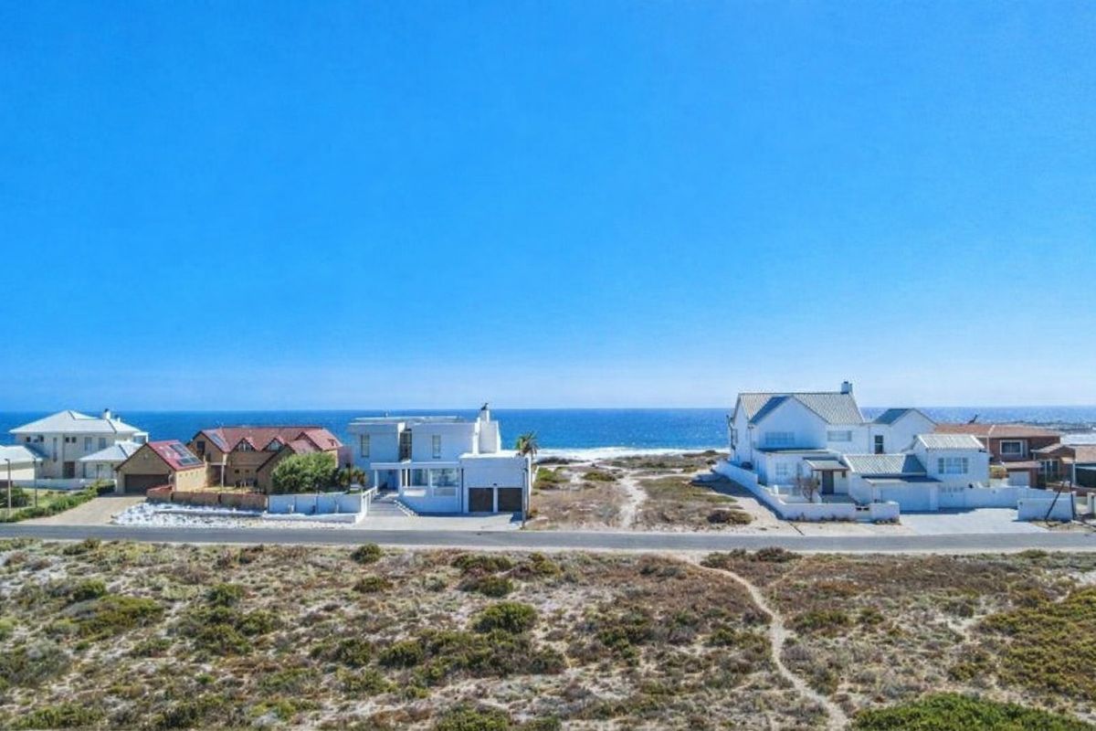 An aerial view of coastal residential properties situated along a paved road with direct ocean views and natural coastal landscape.