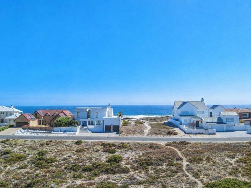 An aerial view of coastal residential properties situated along a paved road with direct ocean views and natural coastal landscape.
