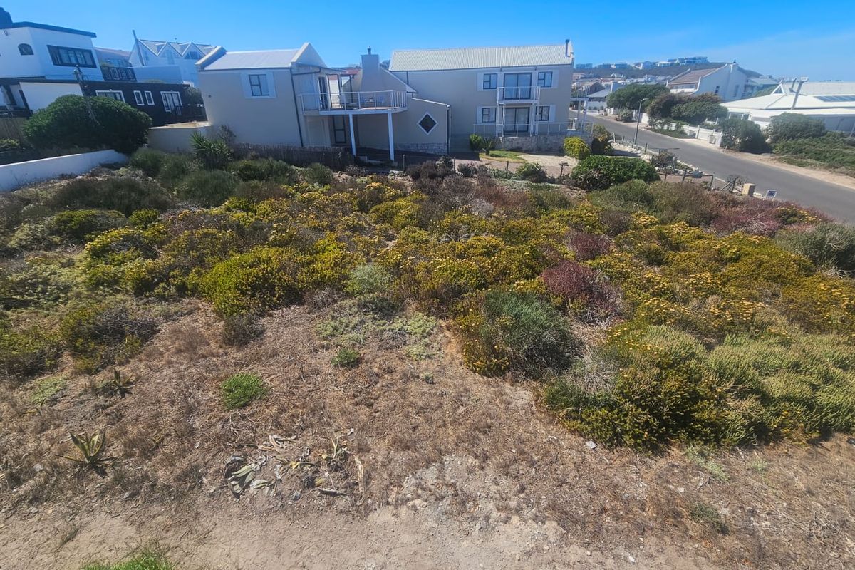 An elevated view of a vacant residential plot featuring natural coastal vegetation, situated in a developed neighborhood with nearby street access.