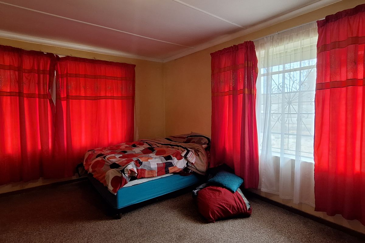 A bedroom featuring carpeted flooring, large windows with security bars, and a simple ceiling light fixture.