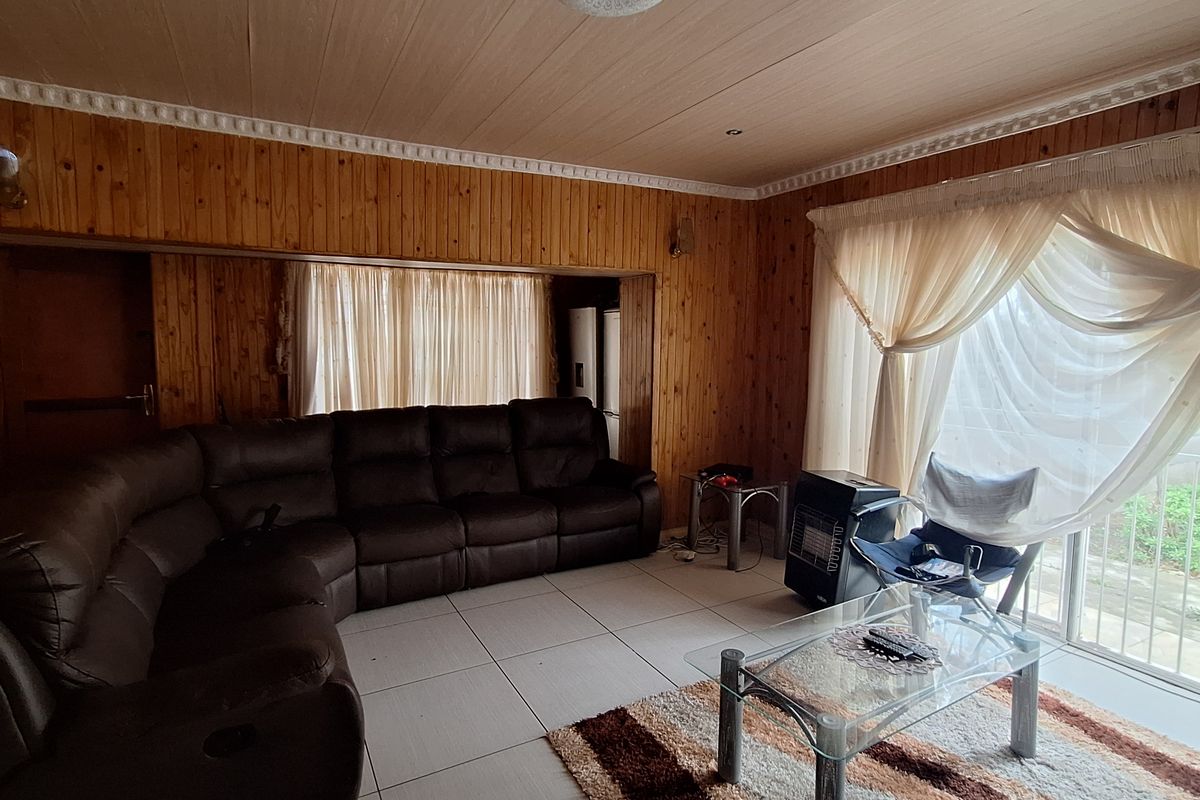 A living room featuring extensive wood-paneled walls and ceiling, large floor tiles, and sliding glass doors leading to an outdoor area.