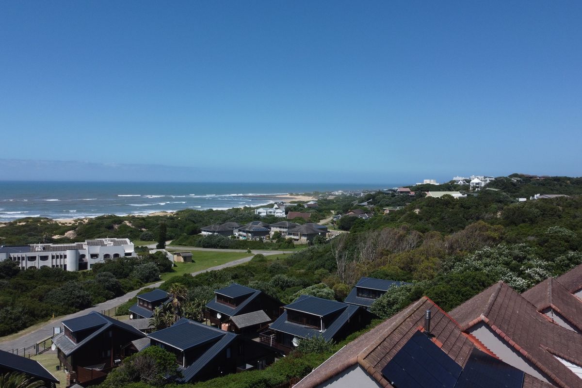 An aerial view of the coastal townhouse complex, showcasing the surrounding landscape, ocean proximity, and residential rooftops with installed solar panels.