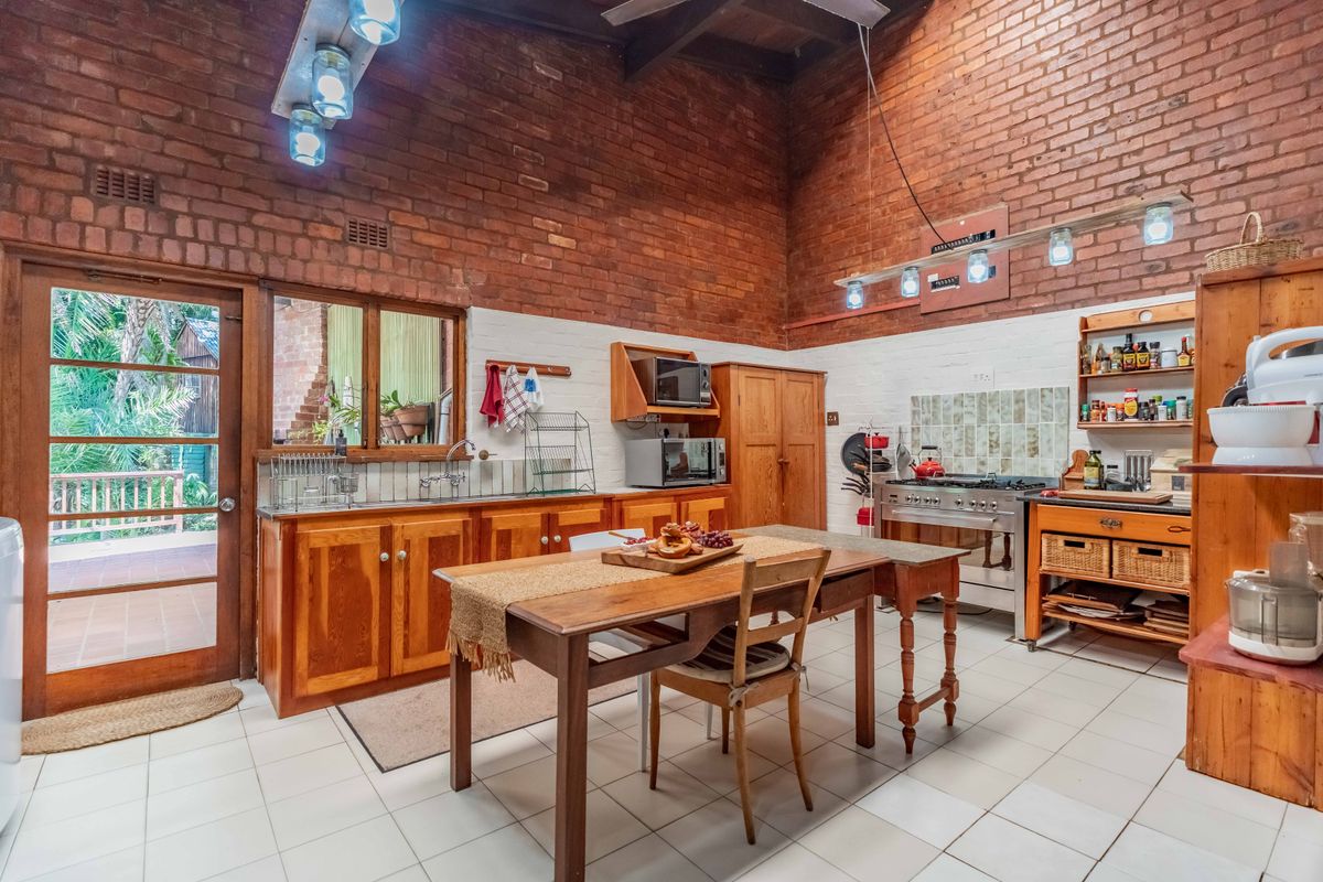 Spacious kitchen featuring exposed brick walls, vaulted ceilings, timber cabinetry, and a stainless steel gas stove, with direct access to an outdoor patio area.