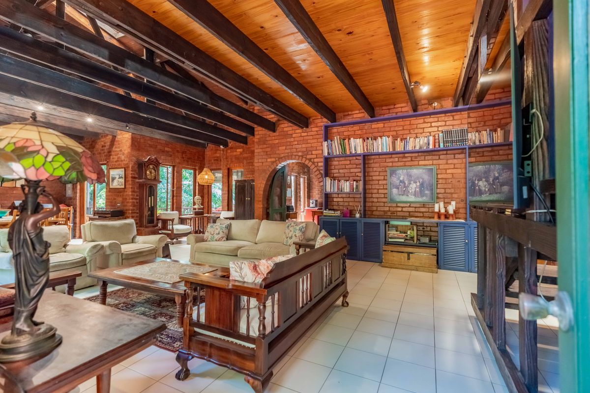 Spacious living room featuring exposed timber ceiling beams, rustic brick walls, tiled flooring, and a large built-in shelving unit.