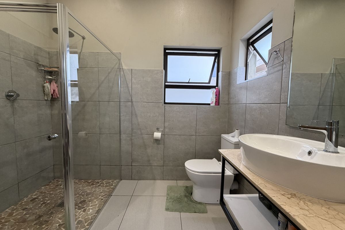 Modern bathroom featuring a glass-enclosed walk-in shower, vessel sink on a stone vanity, and neutral grey wall and floor tiling.