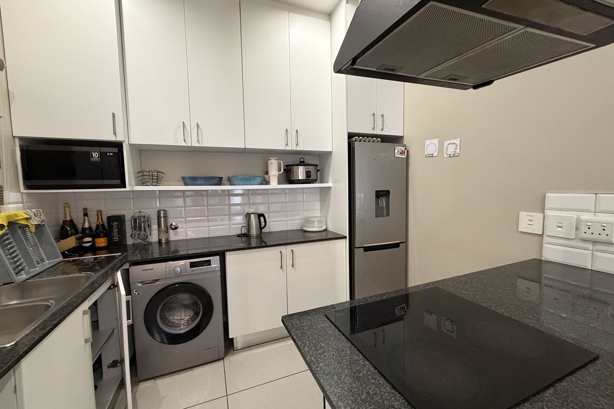 Modern kitchen featuring white cabinetry, dark granite countertops, subway tile backsplash, integrated hob, extractor fan, and built-in microwave with tiled flooring.