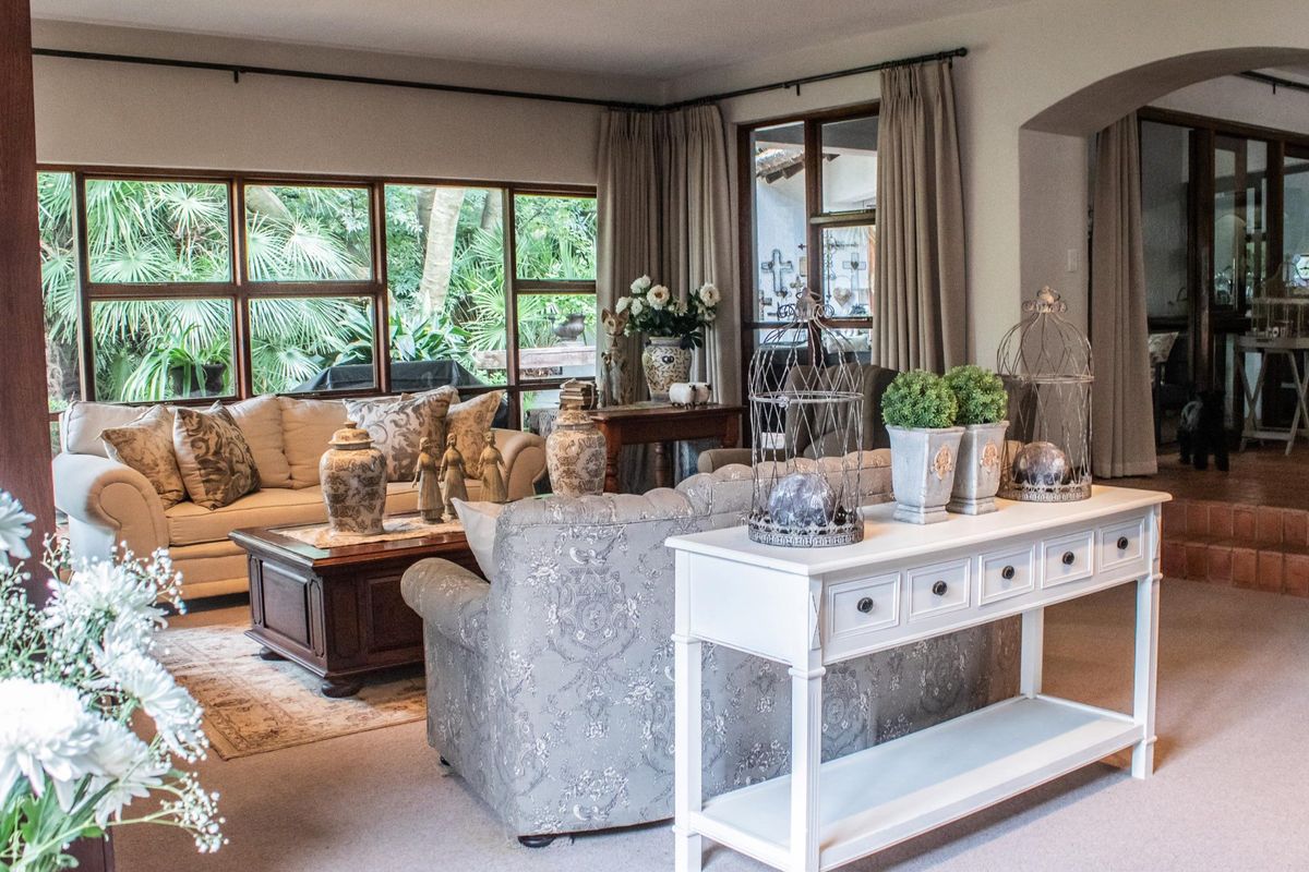 Spacious living room featuring large windows with garden views, carpeted flooring, and an arched entryway leading to an adjacent area.
