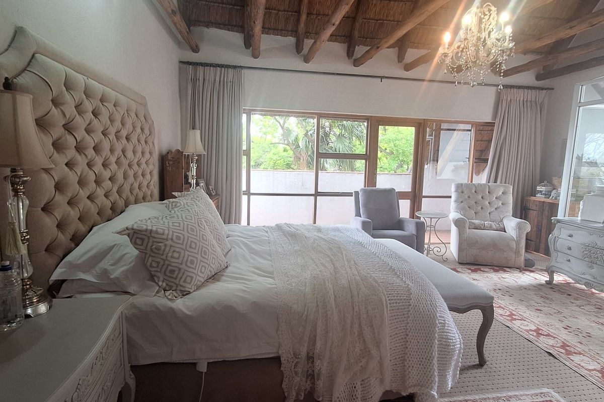Spacious bedroom featuring a high vaulted thatched ceiling with exposed timber beams, large windows, and direct access to an outdoor patio area.