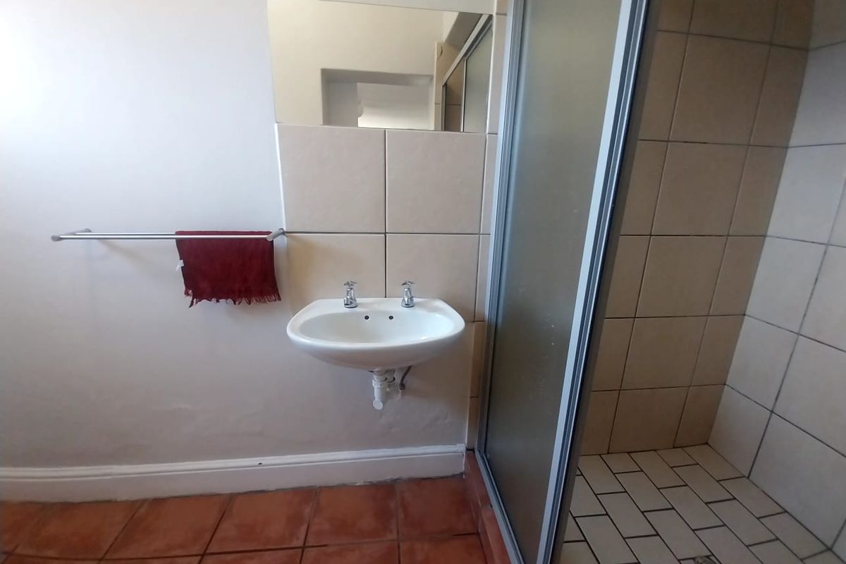 A functional bathroom featuring a wall-mounted basin, a shower enclosure with tiled walls, and terracotta-style floor tiling.