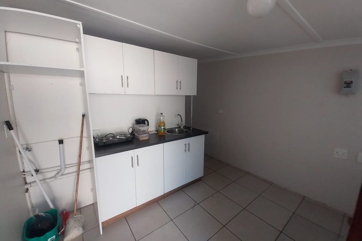 A compact kitchenette featuring white cabinetry, a stainless steel sink, and tiled flooring, suitable for a small utility or studio space.