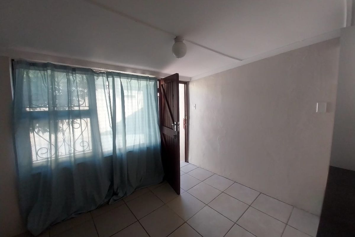 A simple, empty room featuring tiled flooring, a single ceiling light fixture, and a wooden door leading to an exterior space.