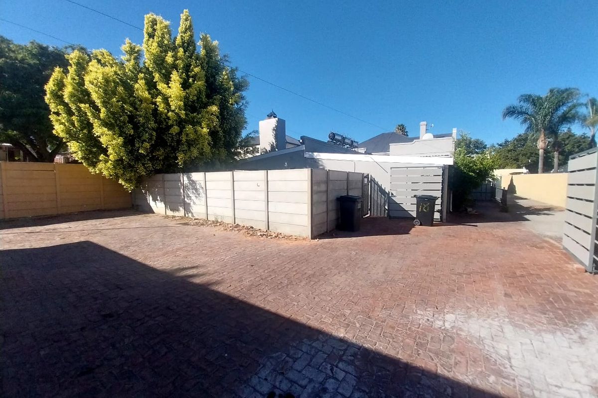 A paved driveway and exterior area featuring perimeter boundary walls and a view of the property's rear roofline and chimney.