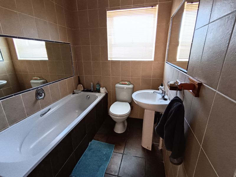 A functional bathroom featuring a built-in bathtub, pedestal basin, and neutral ceramic tiling throughout, offering a clean and practical layout.