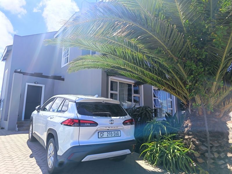 Front elevation of the house featuring a paved driveway, aluminium window frames, and established garden landscaping.