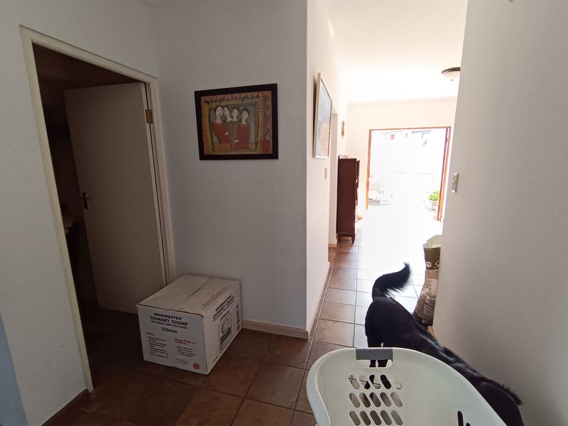 A functional hallway featuring tiled flooring and access to adjacent rooms, leading towards an exterior doorway.