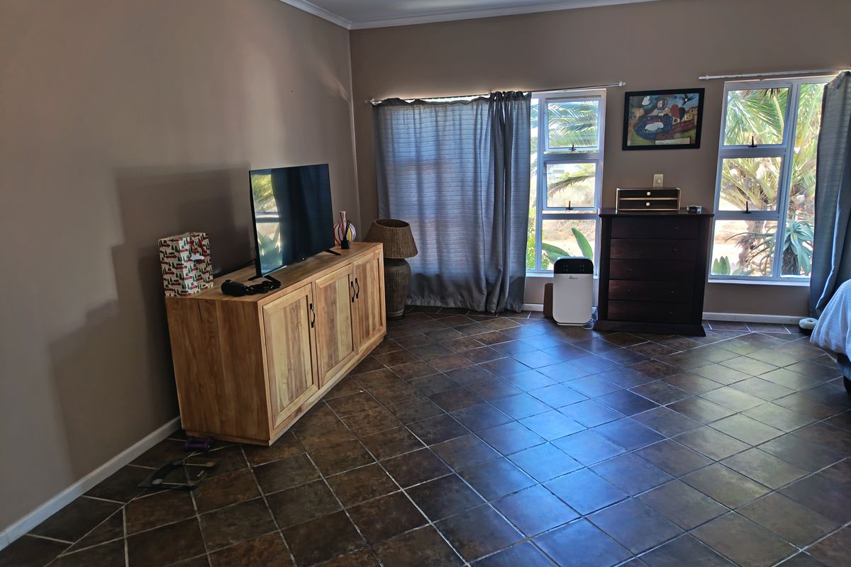 A spacious living room featuring dark ceramic floor tiles and large windows with aluminium frames, providing ample natural light.