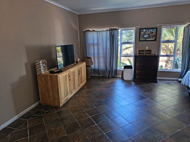 A spacious living room featuring dark ceramic floor tiles and large windows with aluminium frames, providing ample natural light.