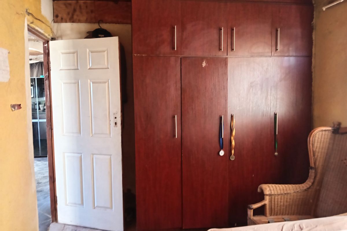A bedroom featuring a large built-in wooden wardrobe and timber ceiling, currently requiring significant cosmetic repairs to the walls and finishes.