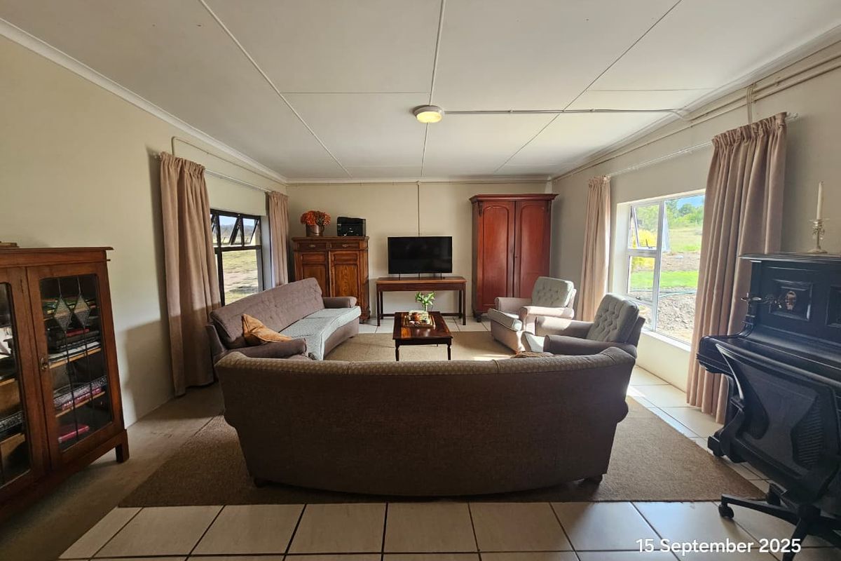 A spacious living room featuring tiled flooring, large windows providing natural light, and exposed surface-mounted electrical conduit along the ceiling.