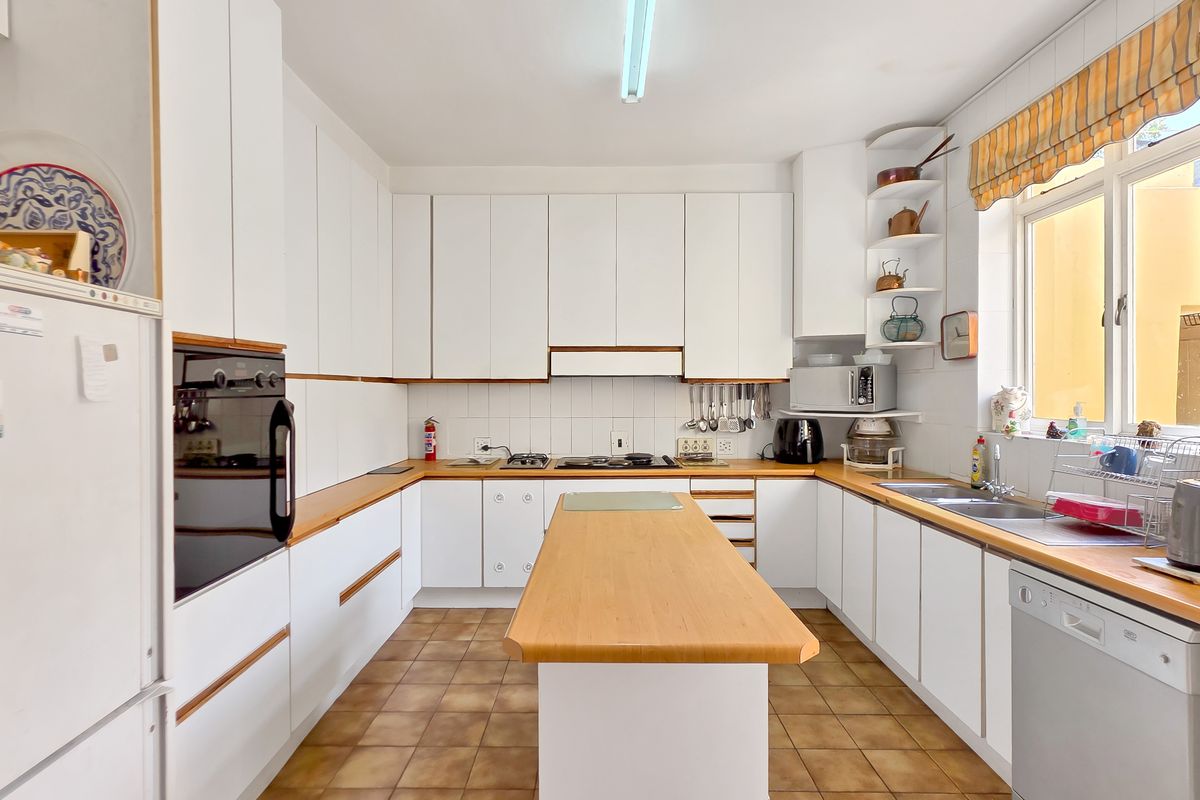 A functional kitchen featuring white cabinetry, wooden countertops, a central island, and tiled flooring, offering a classic layout with ample storage and workspace.