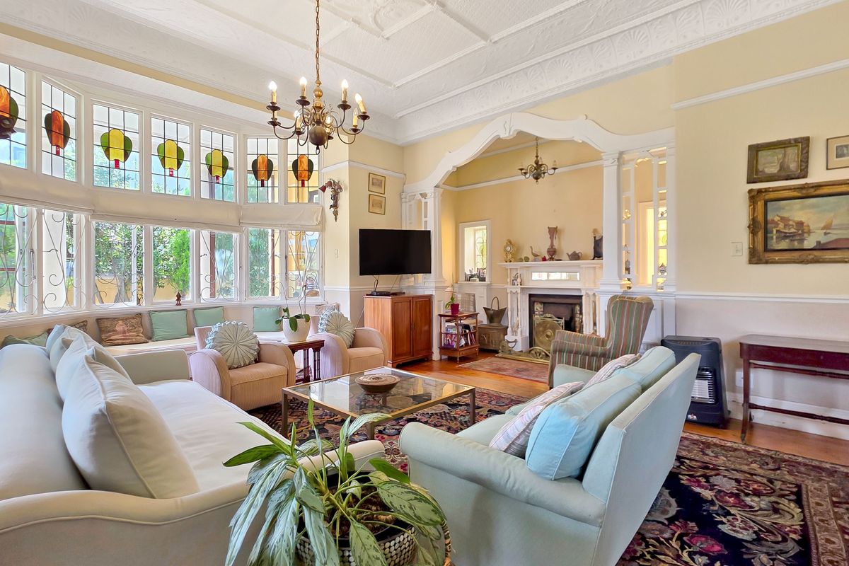 Spacious living room featuring an ornate plaster ceiling, stained glass bay windows, timber flooring, and a classic fireplace with an elegant archway.