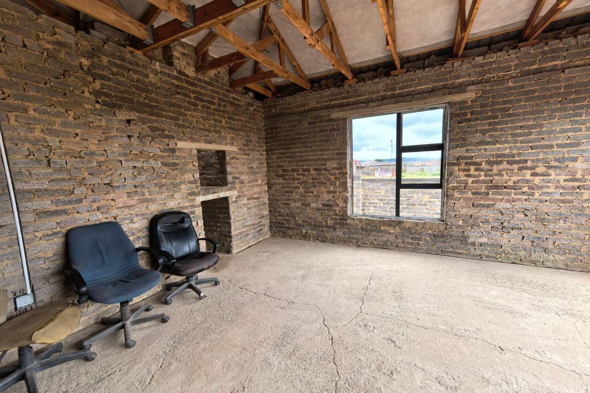 An unfinished room featuring exposed brick walls, timber roof trusses, and a concrete floor, offering a blank canvas for renovation and completion.