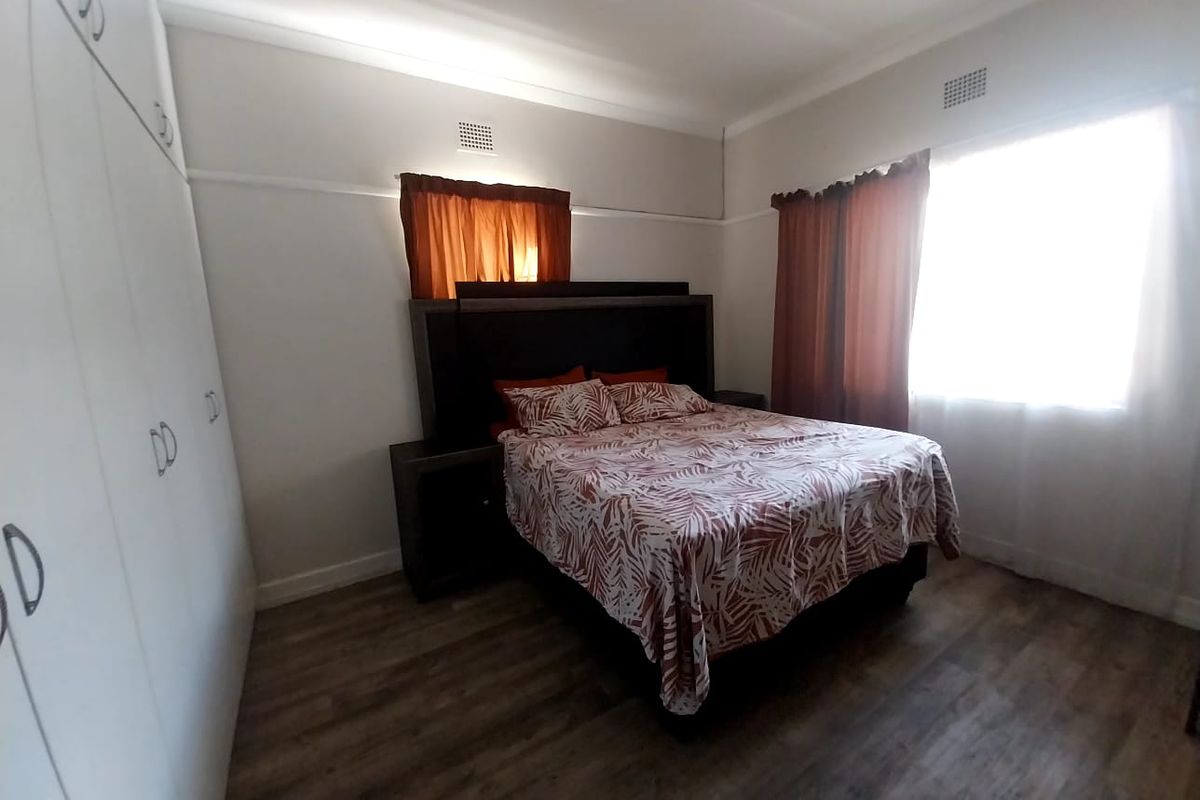 A bedroom featuring built-in cupboards, wood-look flooring, and large windows allowing natural light.