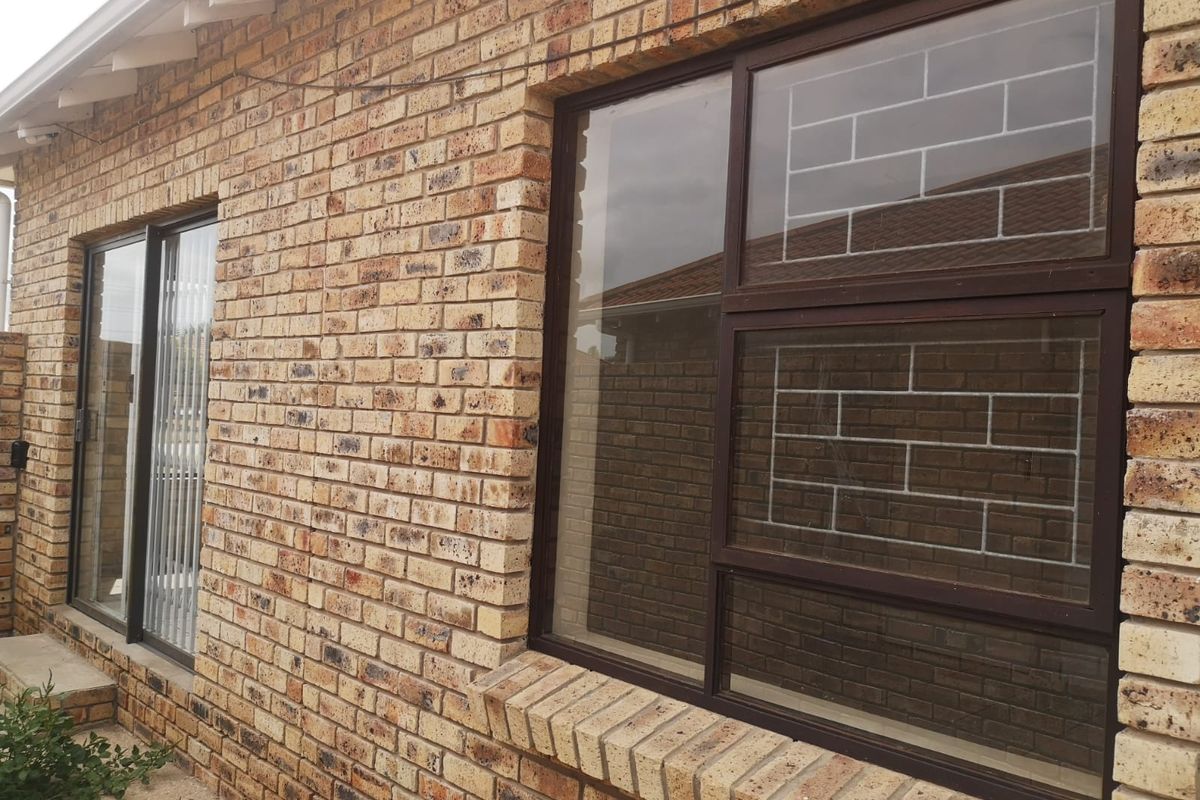 A view of the rear exterior facade featuring face brick construction, aluminium window frames with security bars, and an aluminium sliding door.