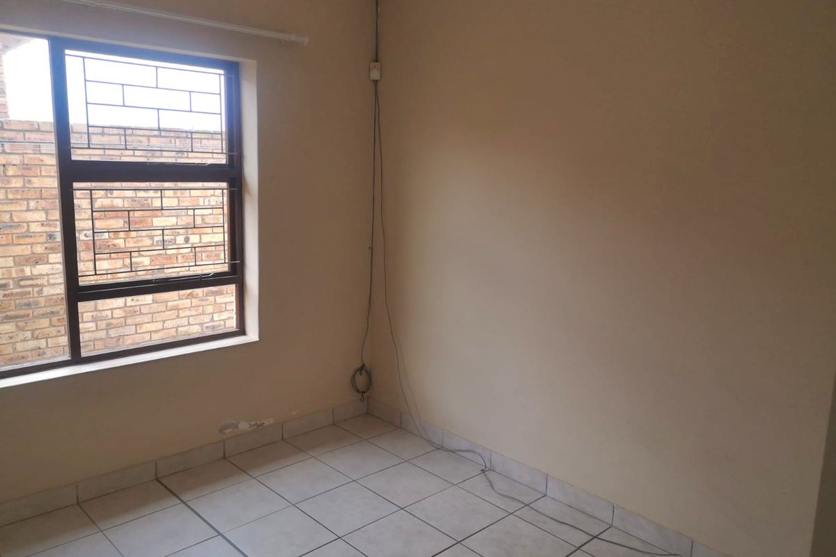 An empty bedroom featuring tiled flooring and a window with security burglar bars, requiring minor cosmetic attention.