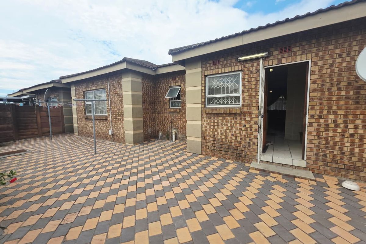 A rear exterior view of a townhouse featuring a paved patio area, face brick walls, and secure window treatments.