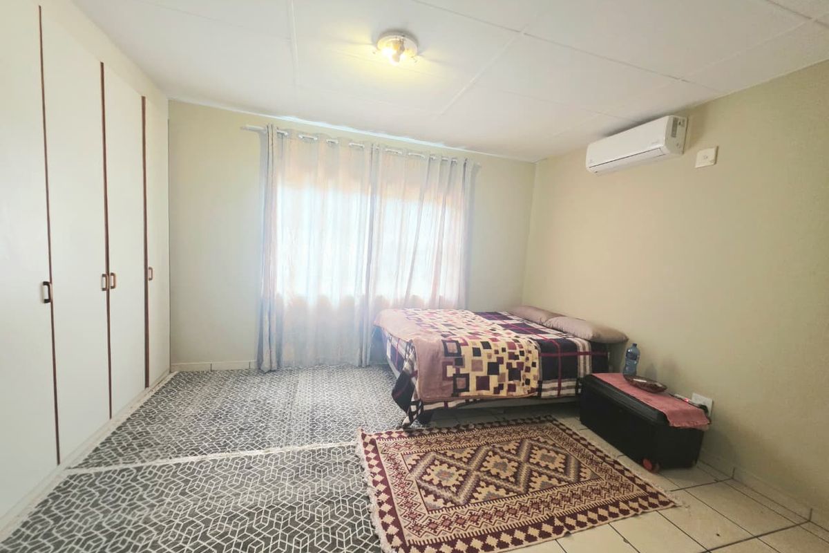 A bedroom featuring built-in cupboards, tiled flooring, and a wall-mounted air conditioning unit.