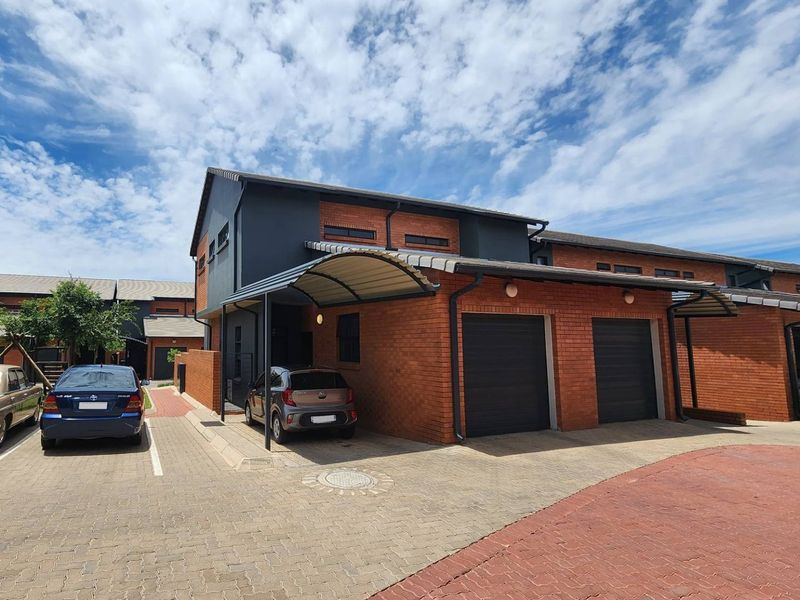 Front view of a modern townhouse featuring a double garage, covered carport, and paved driveway with a combination of brick and dark painted exterior finishes.