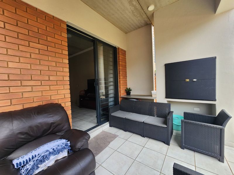 A covered patio featuring tiled flooring, an exposed brick wall, and a built-in braai, providing a functional outdoor entertainment space.