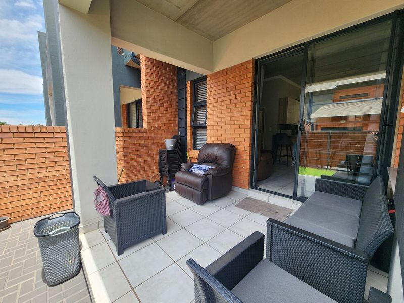 A covered patio area featuring exposed brick walls, tiled flooring, and a large sliding glass door providing access to the interior living space.