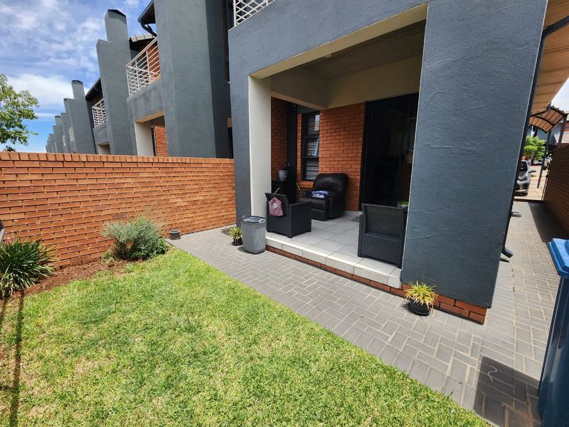 A private rear garden featuring a paved patio area, a small lawn, and a brick boundary wall, attached to a modern townhouse unit.