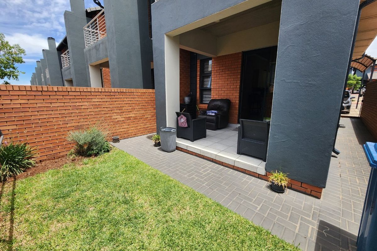 A private rear garden featuring a paved patio area, a small lawn, and a brick boundary wall, attached to a modern townhouse unit.