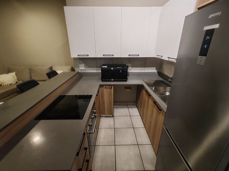 Modern kitchen featuring sleek white and wood-tone cabinetry, stone countertops, integrated electric hob, built-in oven, and a functional breakfast bar layout.