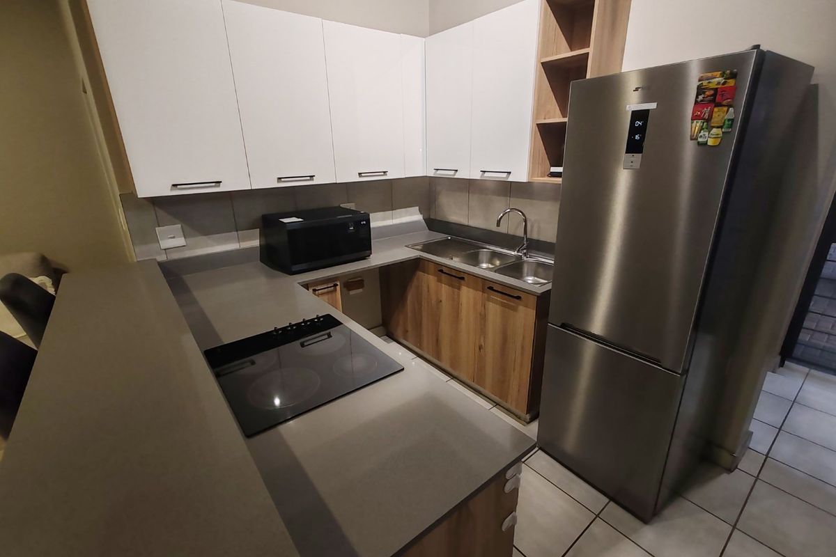 Modern kitchen featuring sleek white and wood-tone cabinetry, stone countertops, a built-in electric hob, and a double bowl sink with tiled flooring.