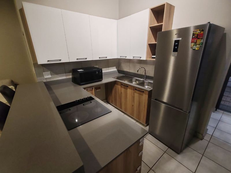 Modern kitchen featuring sleek white and wood-tone cabinetry, stone countertops, a built-in electric hob, and a double bowl sink with tiled flooring.
