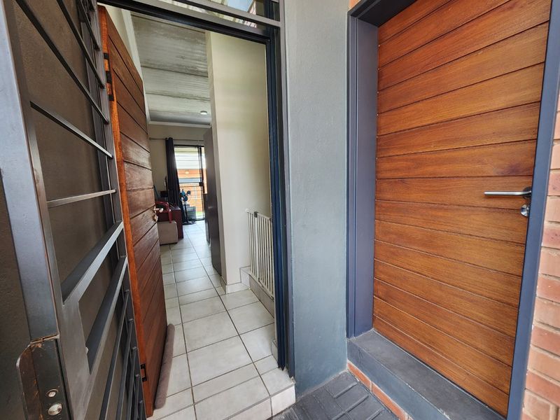 Entrance area featuring a modern timber front door, security gate, and tiled flooring leading into the interior living space.