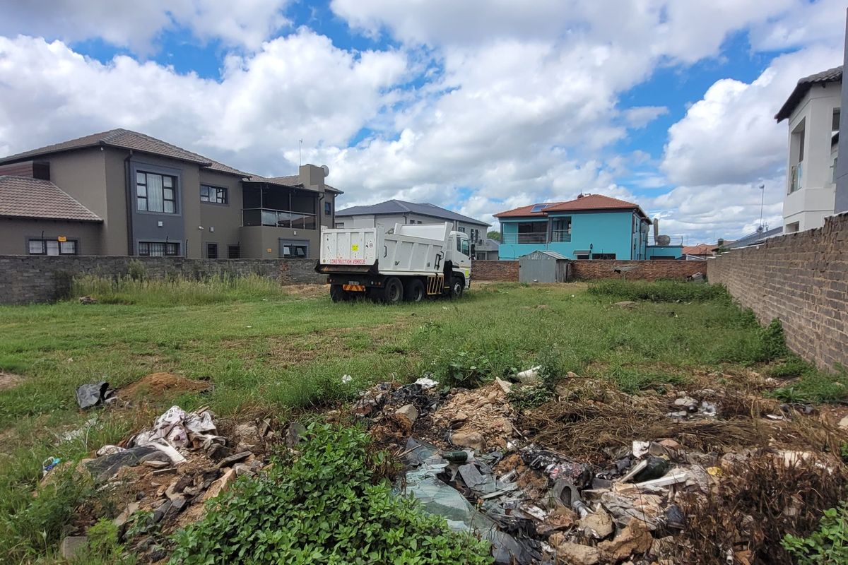 Vacant residential land plot enclosed by perimeter brick walls, currently featuring overgrown grass and accumulated debris.